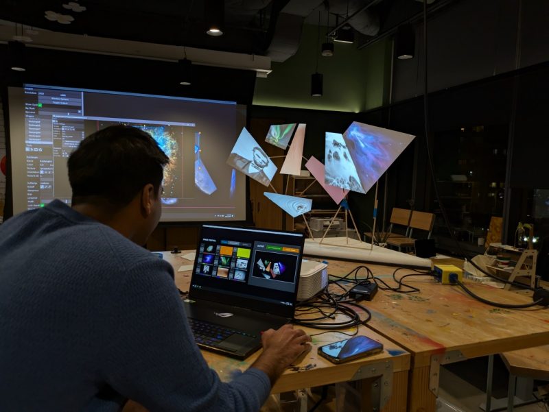 A man aligns projected digital imagery onto suspended geometric forms in the Expressions Lab at Amazon HQ2 during the workshop “Projection Mapping.” Photo by David Franusich for Virginia Tech.