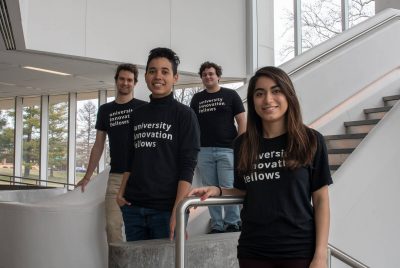 The University Innovation Fellows - four students wearing black t-shirts posing at the bottom of a staircase.