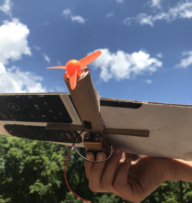 A photo of an airplane made out of cardboard, orange plastic propeller, and battery.