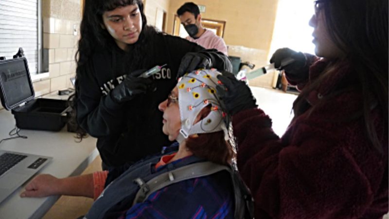 Fig. 2: Shriya Panta, undergraduate researcher in IDPro course, sets up EEG cap with GRAs. 