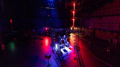People seated inside a lighting and sound setup at Virginia Tech’s Cube performance space, illuminated by red, blue, and purple lights.
